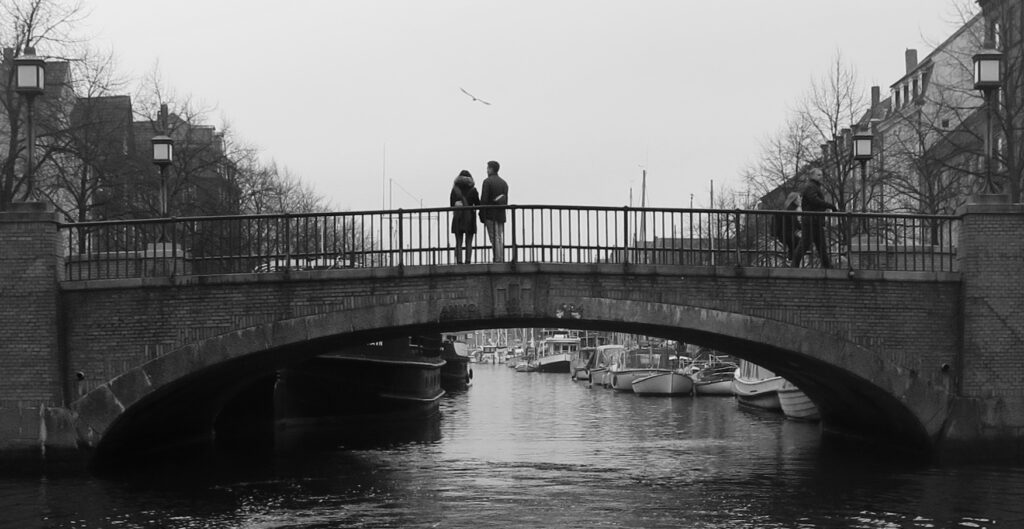 A black and white image of two people on a bridge. Their body language suggests that they are a couple.