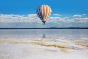 A hot air balloon floating calmly over the sea, the balloon reflected in the water.