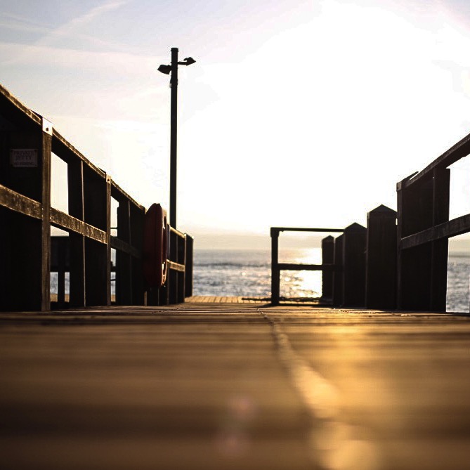 A wooden pier leading out over the sea, with the sun rising.