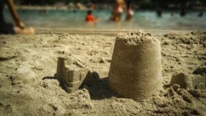 A child's sandcastle on the beach, with people in the distance in the sea.