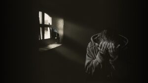 a young person in a darkened room, holding their head in their hands