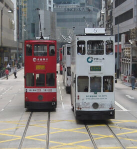 Two trams, on two different routes, one red and one white in a busy city.