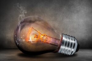 A cracked light bulb, which is glowing dimly and which is releasing smoke, doing the best to give off light