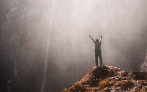 A person standing in front of a waterfall, partially caught in the water mist, looking very happy.