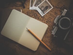 A desk showing an open notebook, yet to be written in, with some pictures and a camera. It looks like someone is about to start a plan.