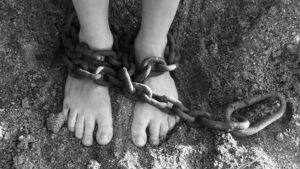 A person with chains around their ankles, burdened and held back