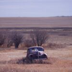 A old car, which is falling apart, stuck in the middle of a field.