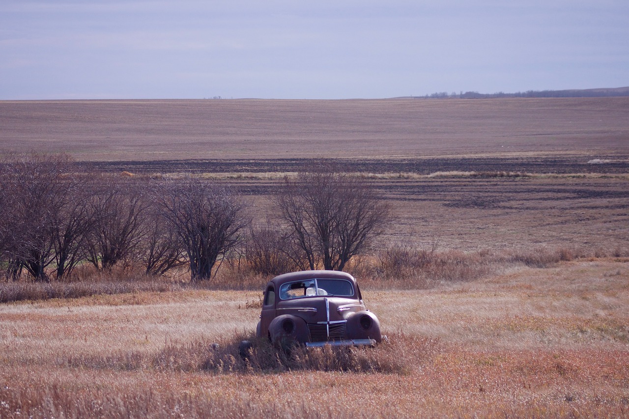 A old car, which is falling apart, stuck in the middle of a field.