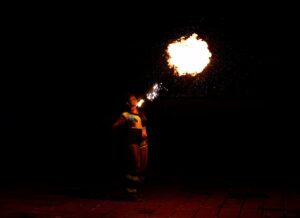 A person blowing fire, with a fireball partially lighting them up