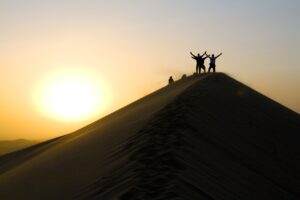 Three people celebrating their achievements on top of a hill, with the sun rising in the background