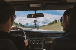 Two people driving, with a view of the road ahead.
