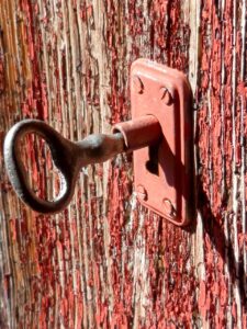 A rustic key in an old lock, which is fitted to faded red wood