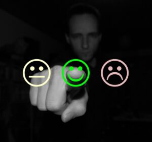 A man stands in the background of a black and white photo. He is slightly out of focus. His finger is pointing forward to an icon of a smiley face. He has picked the smiley face instead of the unhappy or neutral face. This is his feedback and his choice.