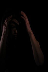 A very dark image of a fearful person holding their head.