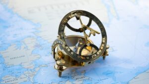A brass compass sitting on a map of the world. The compass is showing which direction to take.