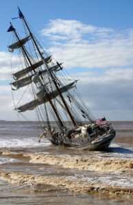 A old ship, with tall masts and no open sails, has run aground on the beach. No direction, just drifting along.