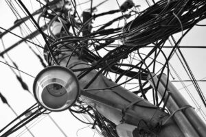 A black and white photo of multiple cables attached to a pole. It is absolute chaos.