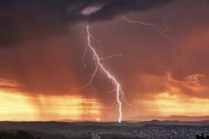 A bolt of lightning striking the ground, with a sunlight sky in the distance and dark clouds in the fore.