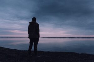 A person standing alone beside a calm lake.