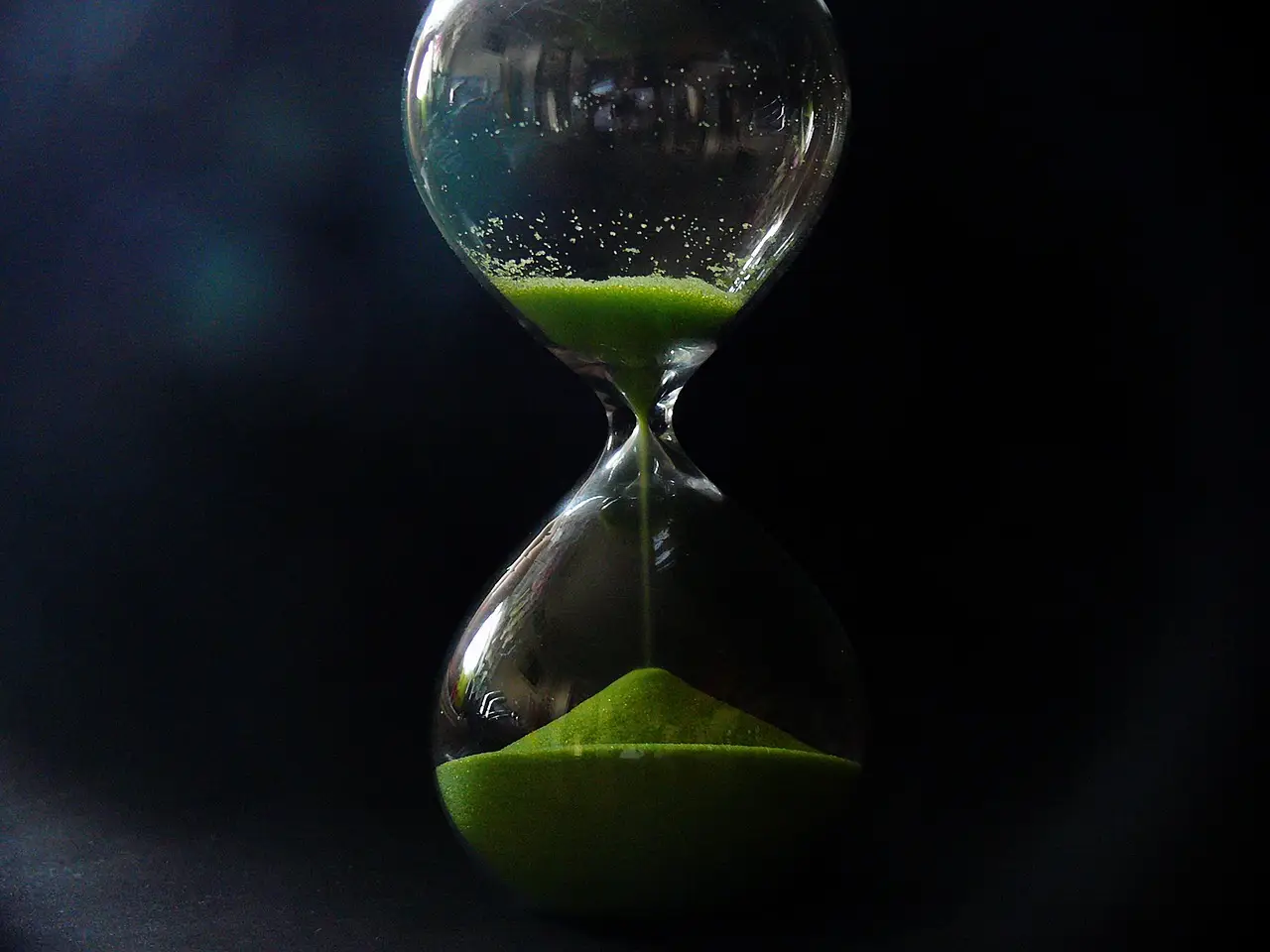 An hourglass, with green sand slowing passing, like the passing of time.