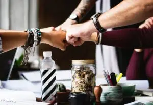 A group of people, bumping fists, all part of a team working together.