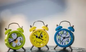 Three old fashioned alarm clocks, with bells on top, in three colours; green, yellow, and blue.