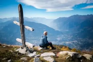 A woman sits atop a mountain, admiring the view.