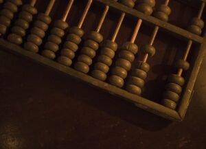 Close-up of an antique wooden abacus with green beads on vertical rods in warm light surface visible beneath.